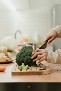 Close-up of hands slicing fresh organic broccoli on a kitchen counter, perfect for food preparation themes.