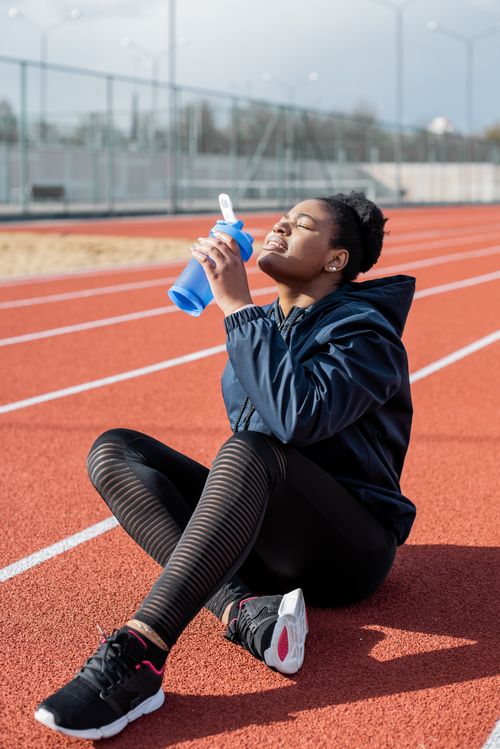 Free A woman in athletic wear hydrates with a water bottle on a sunny running track day. Stock Photo