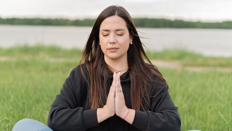 A serene woman practicing meditation outdoors near a lake, promoting wellness and relaxation.