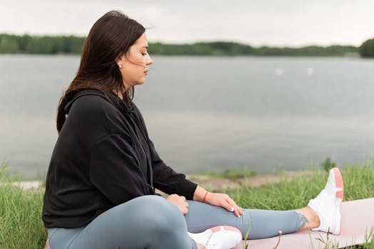 Woman meditating outdoors by a tranquil lakeside, fostering health and wellness.