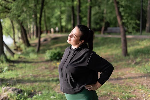 A woman in activewear takes a moment to stretch in a sunny, green park setting, promoting wellness and fitness.