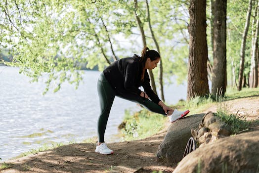 A woman in sportswear stretches by a serene lake surrounded by trees, embracing nature and fitness.