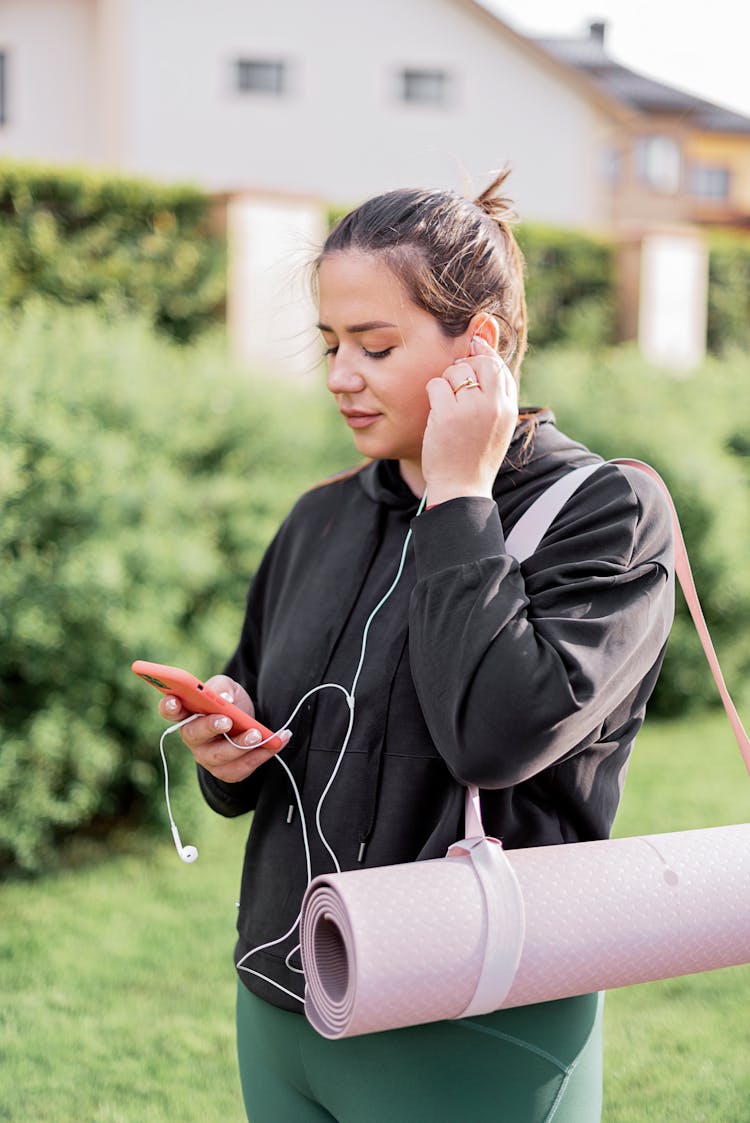 Woman In Black Jacket Holding A Smartphone With Earphone