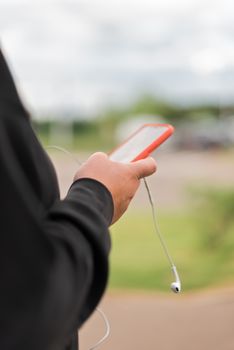 Close-up of a hand holding a smartphone with earphones outside.