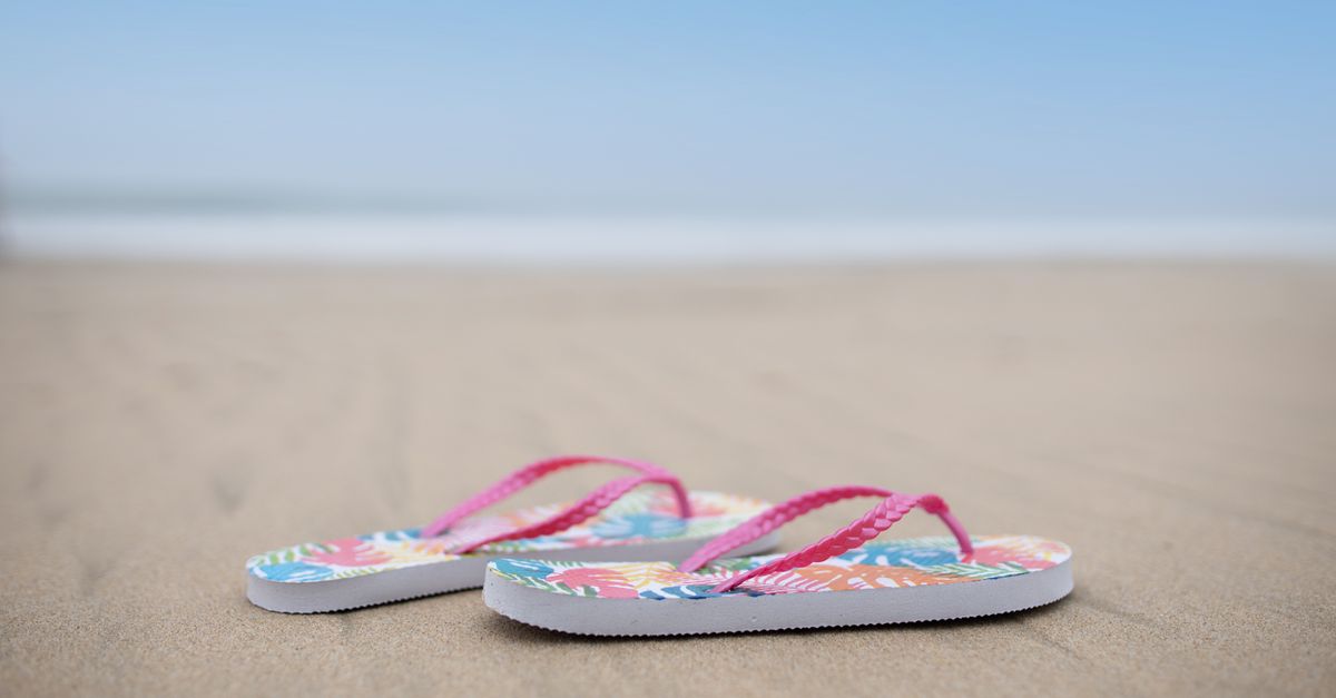 Colorful flip flops resting on a sandy beach with a blue sky overhead, capturing a perfect summer vibe.