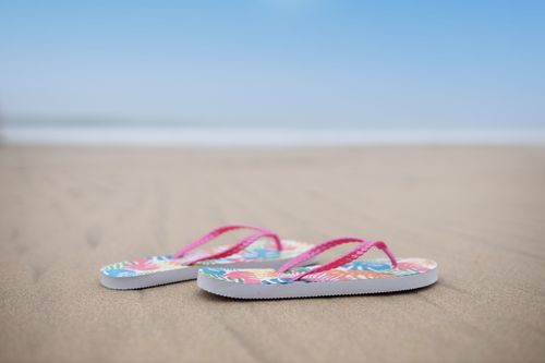 Free Colorful flip flops resting on a sandy beach with a blue sky overhead, capturing a perfect summer vibe. Stock Photo