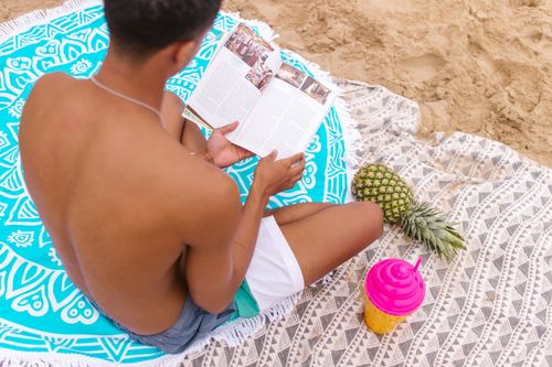 Free A man enjoys a summer day on the beach reading a book, complete with a tropical pineapple drink. Stock Photo