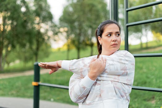 Woman stretching her arms in a park during an outdoor workout session in a lush green setting.