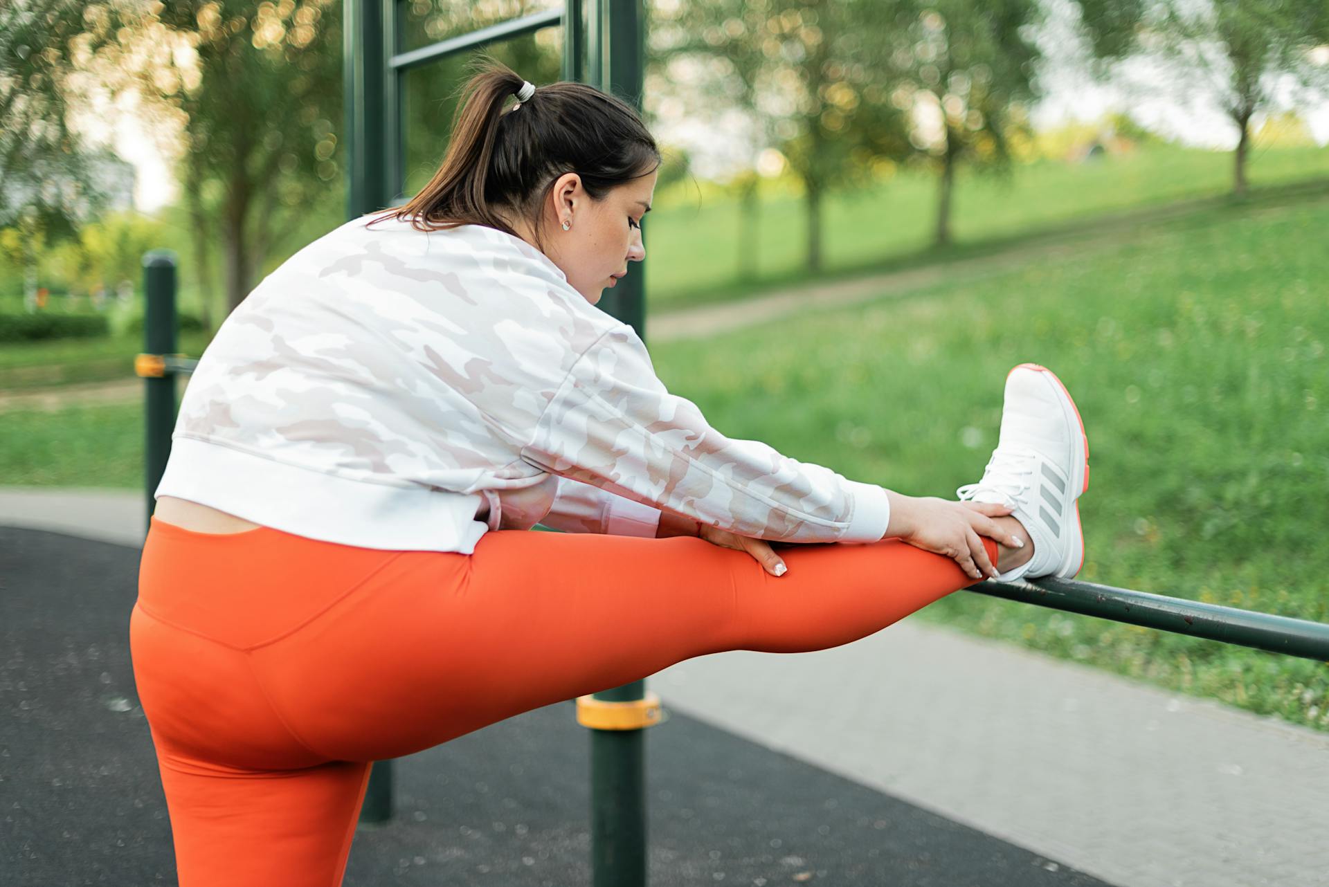 Plus size woman stretching in park wearing orange leggings, promoting active lifestyle and wellness.