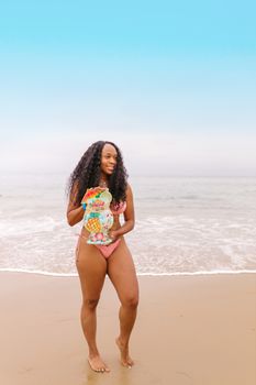 Smiling woman in bikini holds a colorful placard while standing on a sandy beach.