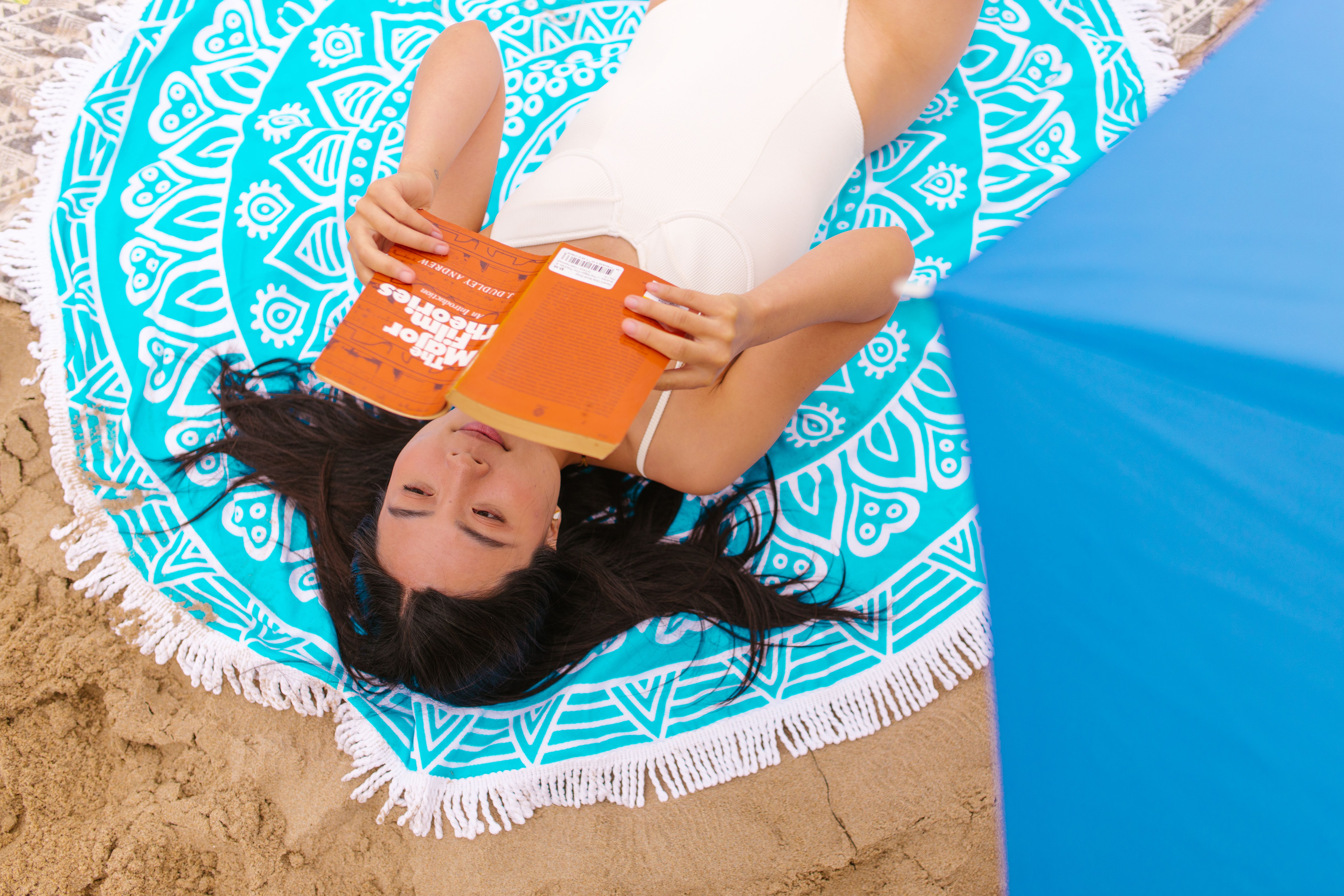 Woman sunbathing and reading on a vibrant beach towel, enjoying a peaceful summer day.