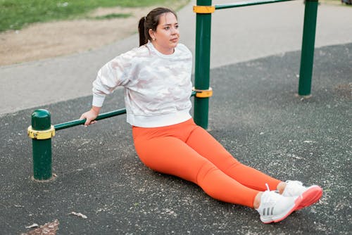 A Woman in an Orange Yoga Pants Stretching with a Metal Bar