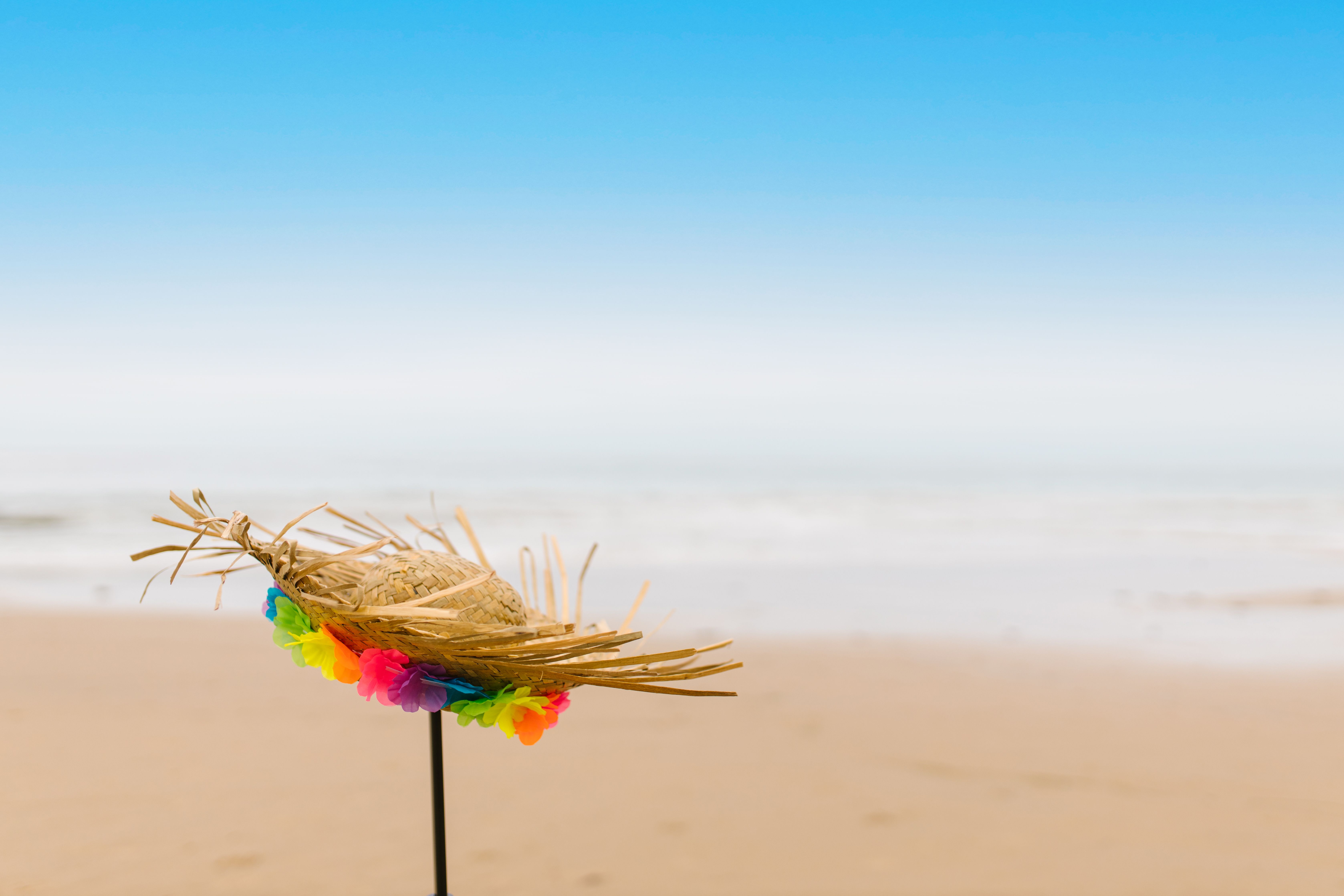 a wide-brimmed hat on a white sand beach, clear blue ocean background in Okinawa