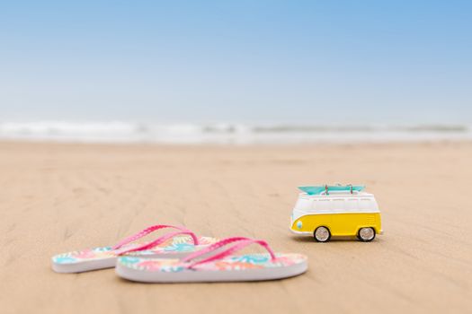 Vibrant flip flops and a playful toy van on a sandy beach, perfect for vacation vibes.