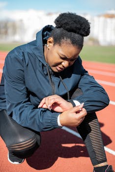 A woman in activewear checks her watch on a sunny day at the running track.