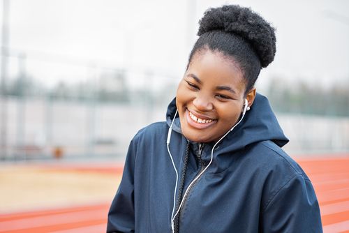 Free A joyful woman in a blue jacket enjoys music with earphones while standing on a track. Stock Photo