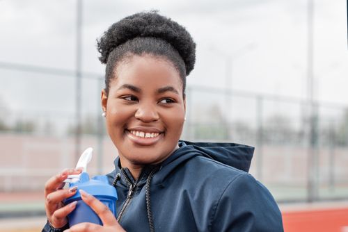 Free Happy woman in a jacket enjoying a refreshing drink outdoors. Perfect for lifestyle and health themes. Stock Photo