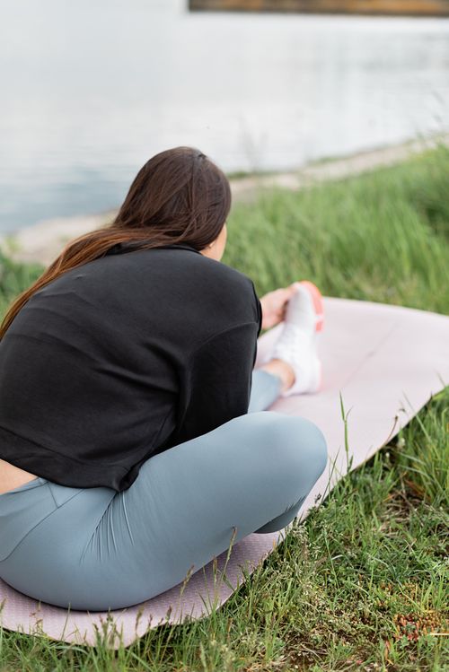 Free A woman in activewear stretches on a yoga mat by a tranquil lakeside, enjoying outdoor exercise. Stock Photo