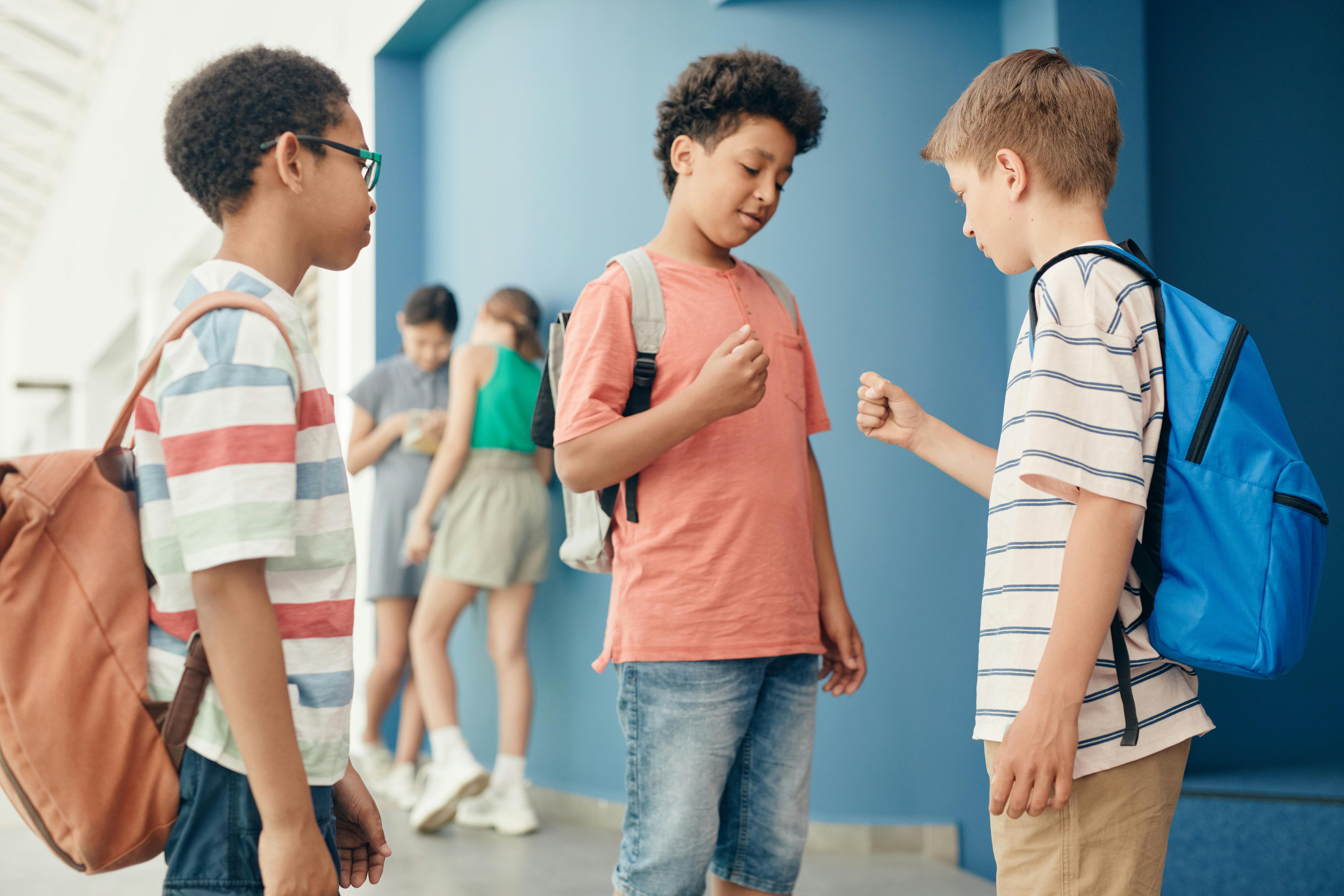 Three boys enjoy a game of rock paper scissors in a school hallway during break time.