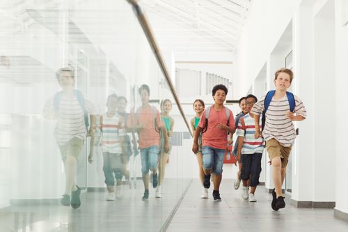 Free Group of diverse kids joyfully running in a bright school hallway. Stock Photo