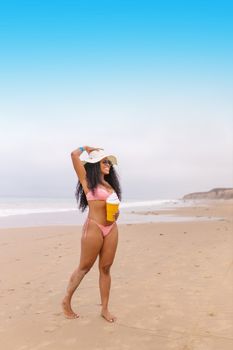A woman in a bikini enjoying a sunny day at the beach with a drink in hand.