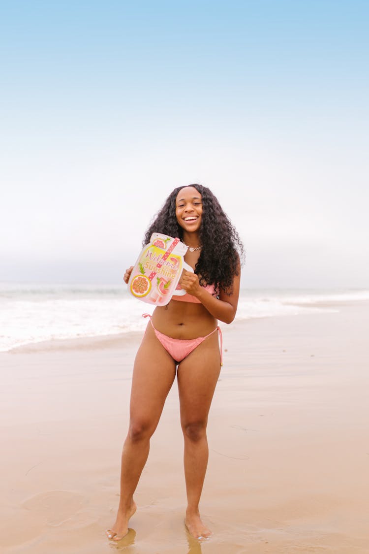 A Woman In Bikini Sanding On The Beach Holding A Colorful Banner