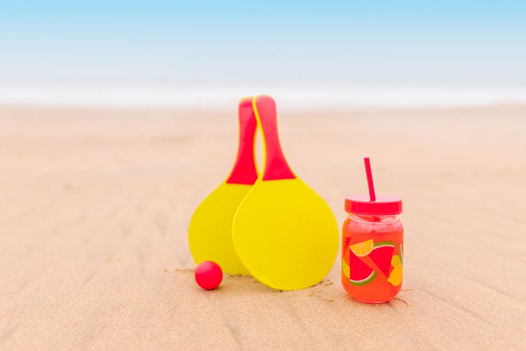 Mason Jar With Juice And Colorful Ping Pong Rackets On Sand