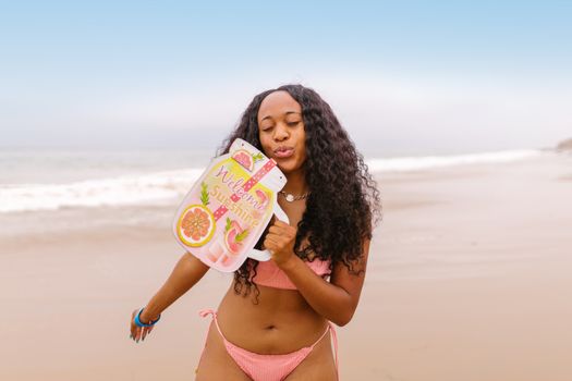 A woman in swimwear enjoys a sunny beach day, holding a refreshing drink sign that says 'Welcome Sunshine'.