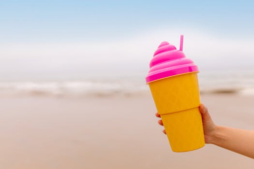 Vibrant plastic ice cream tumbler held by a hand on a sunny day at the beach.