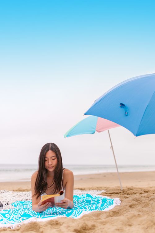 Free A woman comfortably reads a book under a beach umbrella on a sunny day. Stock Photo