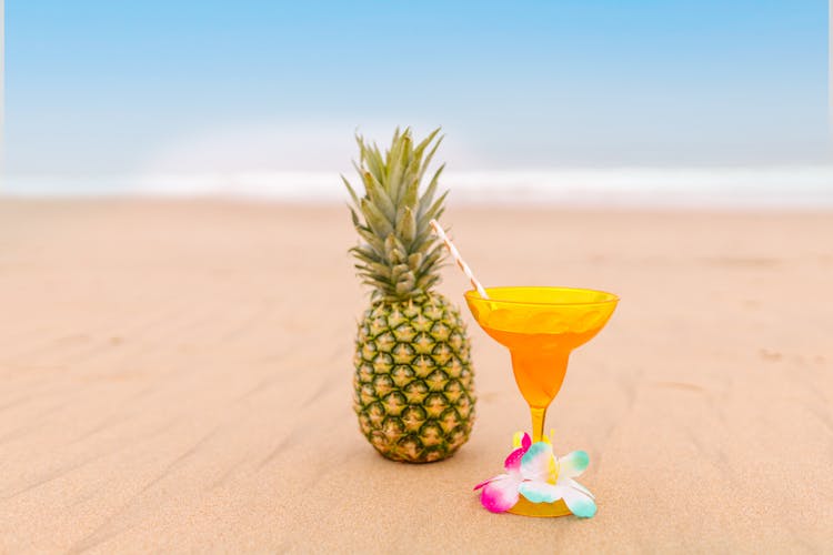 Cocktail Beside A Pineapple On Beach Sand