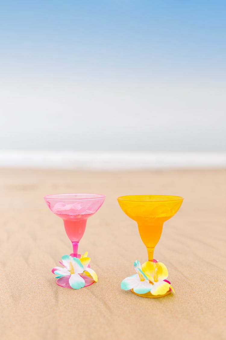 Cocktail Glasses Decorated With Flowers On Beach By Sea Shore