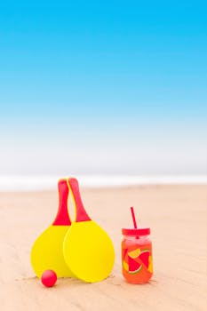 Vibrant beach setting featuring paddles and a tropical drink against a clear blue sky.