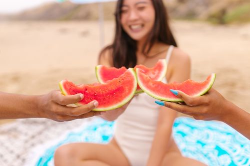 Free A vibrant scene capturing people enjoying watermelon slices on a sunny beach day, embracing summer's delights. Stock Photo