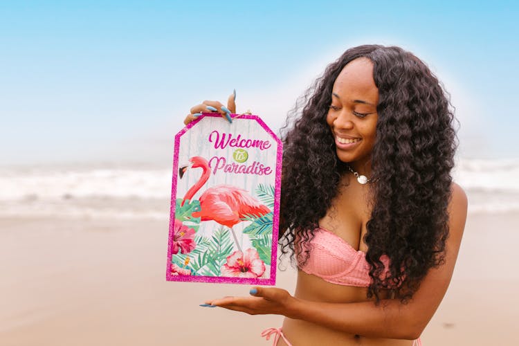 A Woman In A Bikini Holding A Sign At The Beach