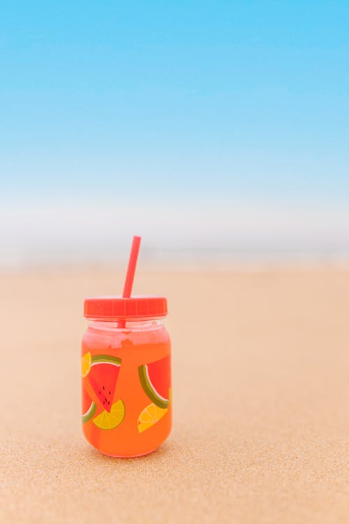 Close-up of a Drink in a Bottle with a Straw Standing on a Beach 