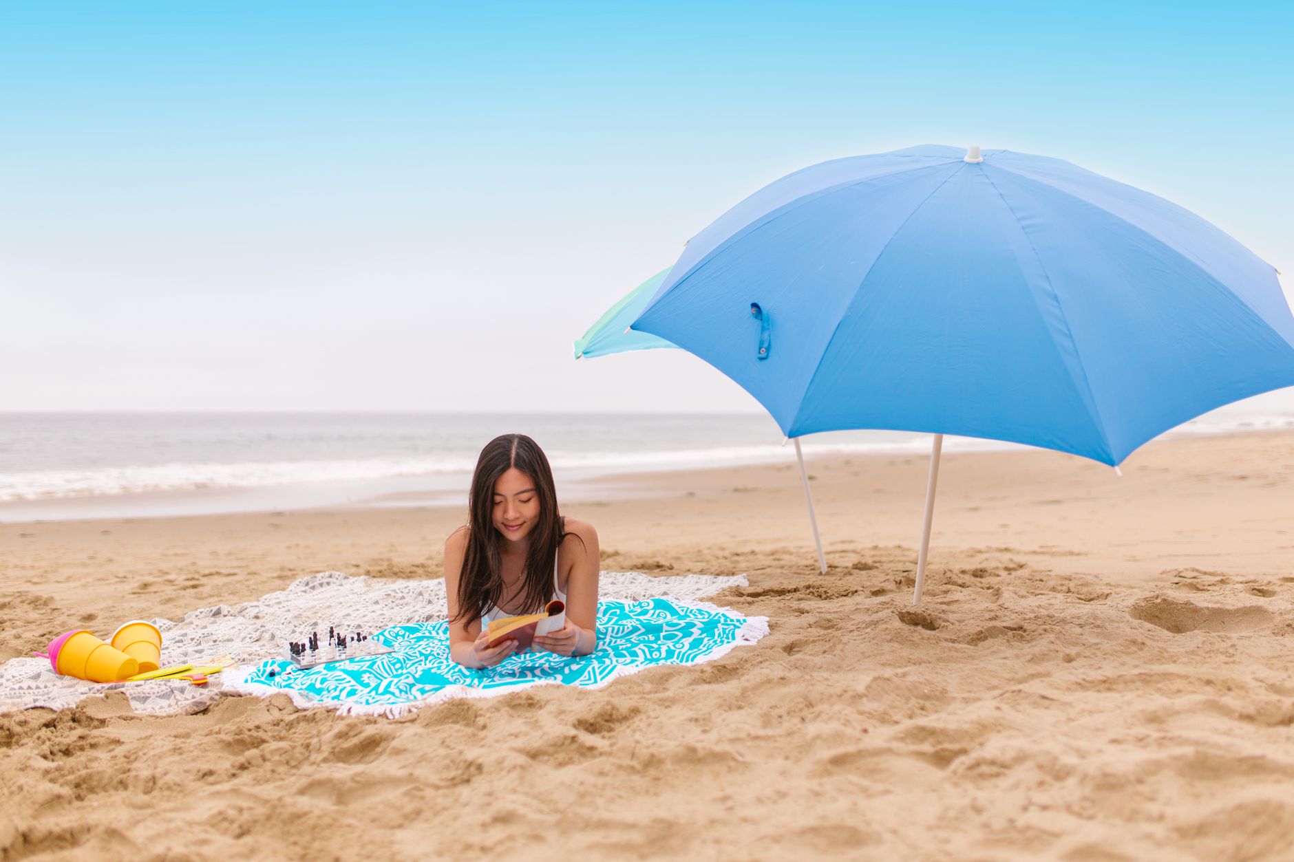 Woman reading a book on a sandy beach under a blue umbrella