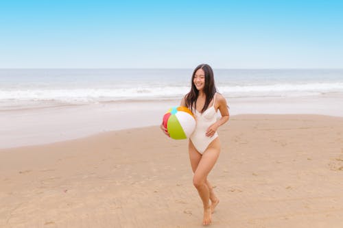 Free Woman in White Bikini Holding Yellow and Green Inflatable Ball on Beach Stock Photo