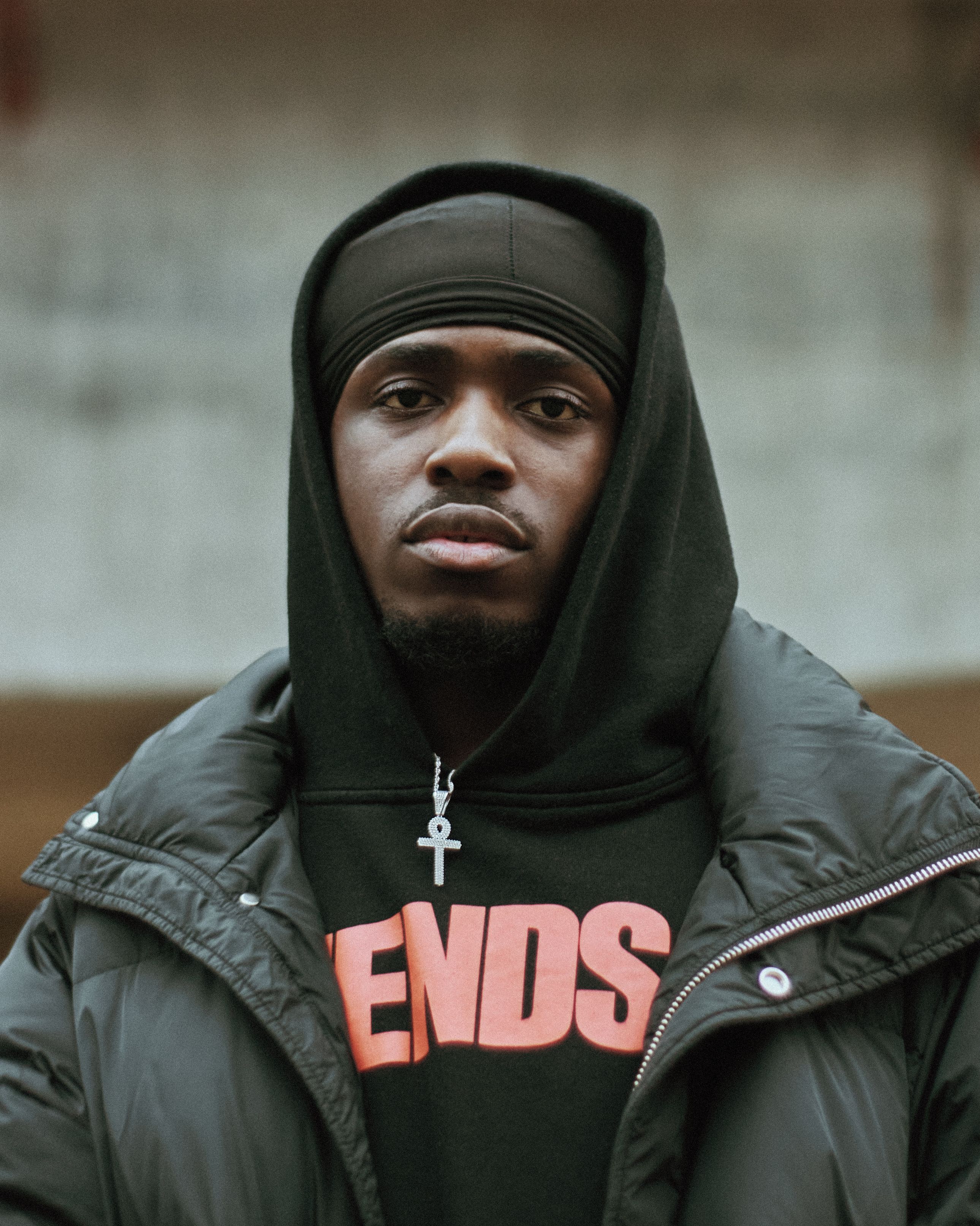 Portrait of a young black man in a stylish hoodie and jacket, London backdrop.