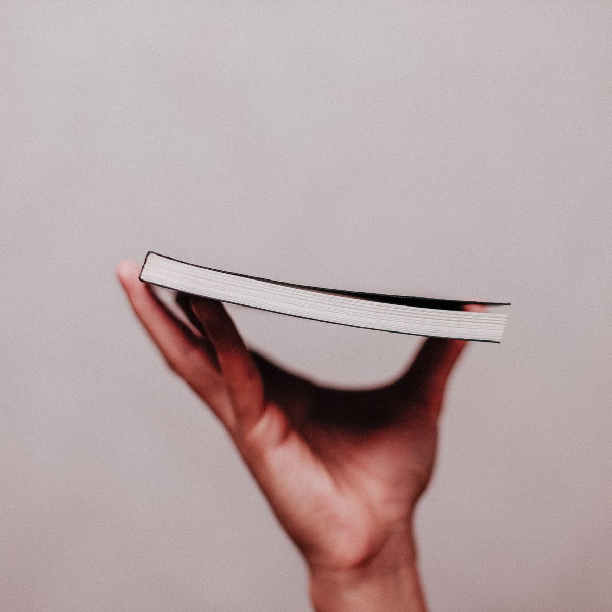 A closed hardback held edge-on against a plain wall &mdash; photograph by Luis Quintero on Pexels