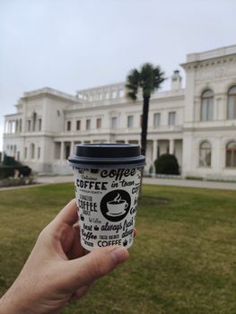 Hand holding a coffee cup in front of a classic historical building outdoors.