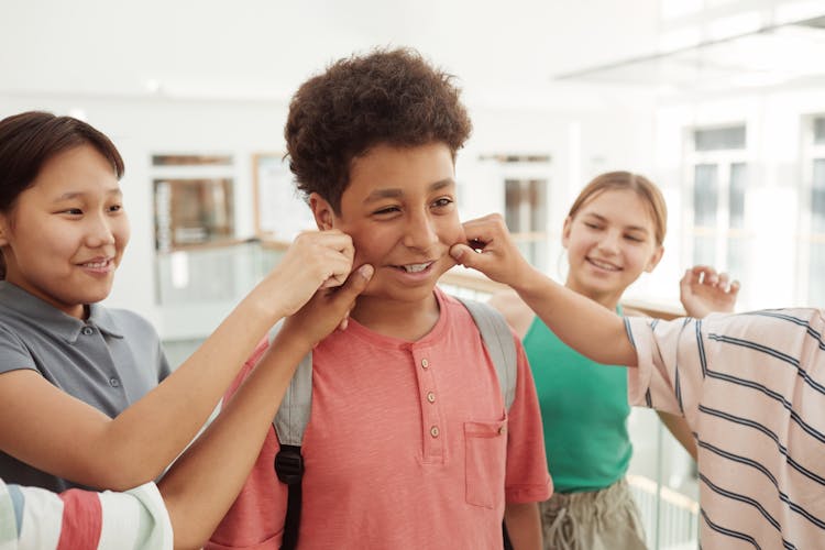 Children Pinching A Young Boy's Cheeks