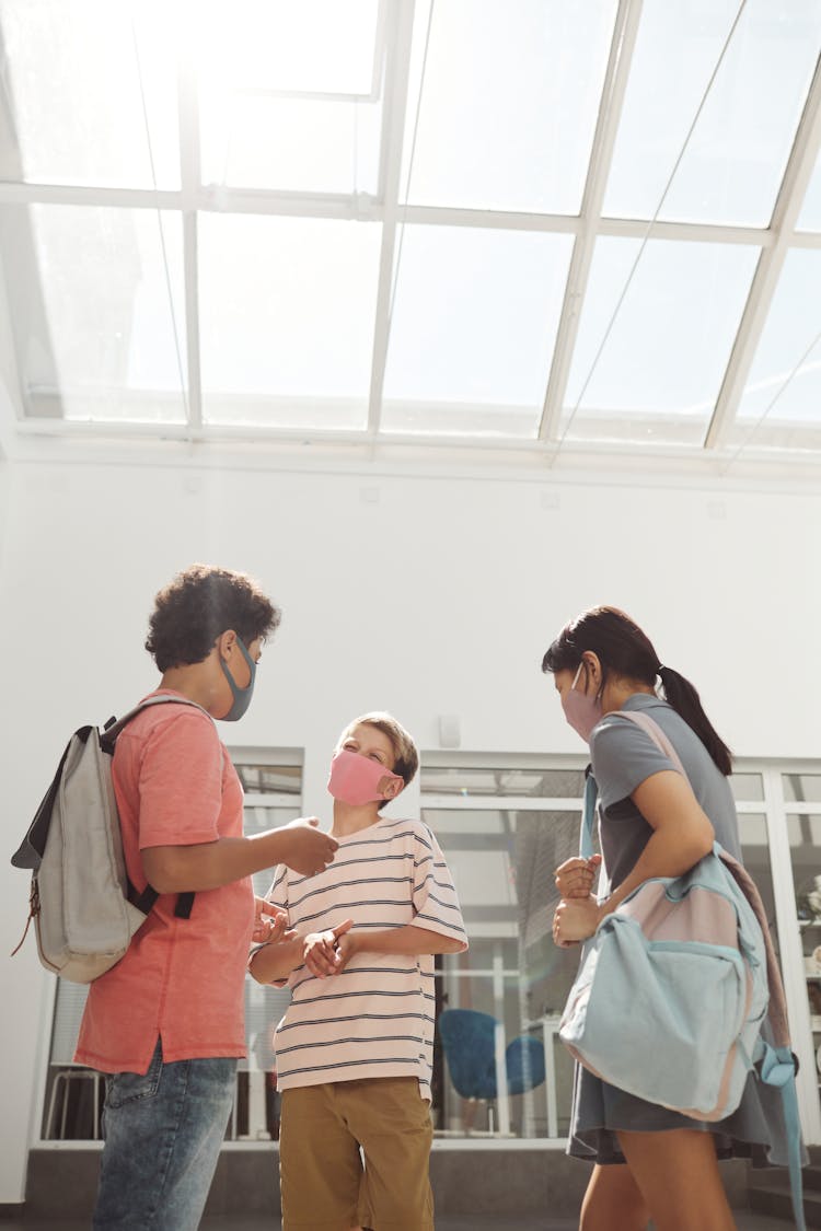 Group Of Schoolkids In Face Masks Standing In The School Hallway And Talking 