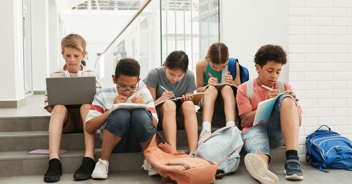 A group of school students sitting in a hallway, focused on studying and writing.