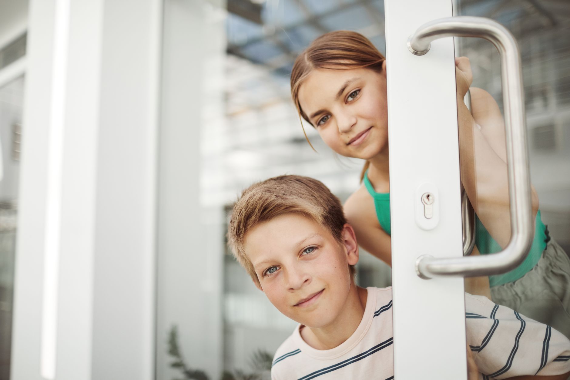 Two kids peeking through a glass door, exuding curiosity and playfulness.