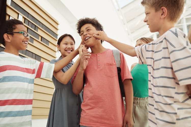 Boy Getting His Cheeks Pinched By His Friends At School 