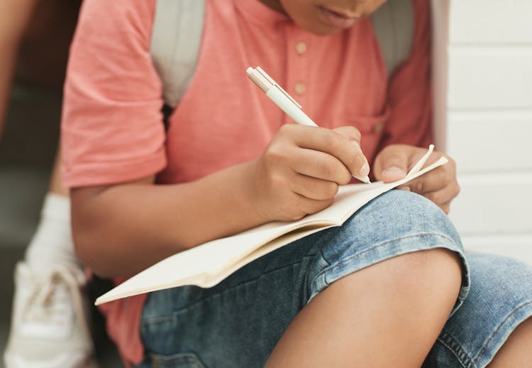 A Teenager Writing On A Notebook