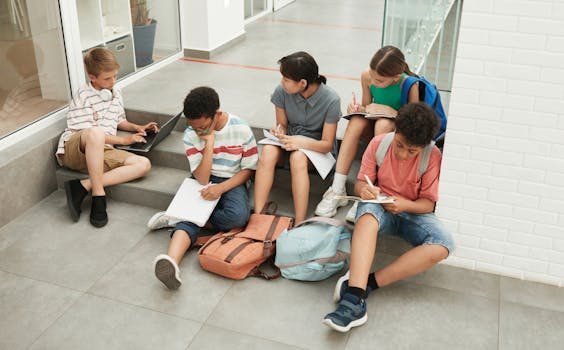 Five teenagers studying together with laptops and notebooks indoors.