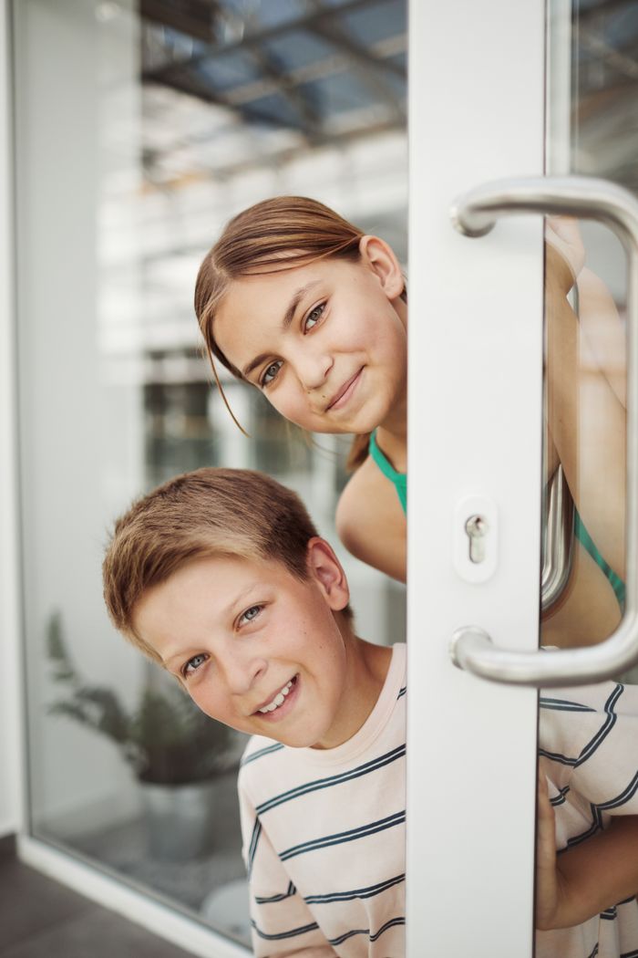 Two children smiling and peeping through a school door