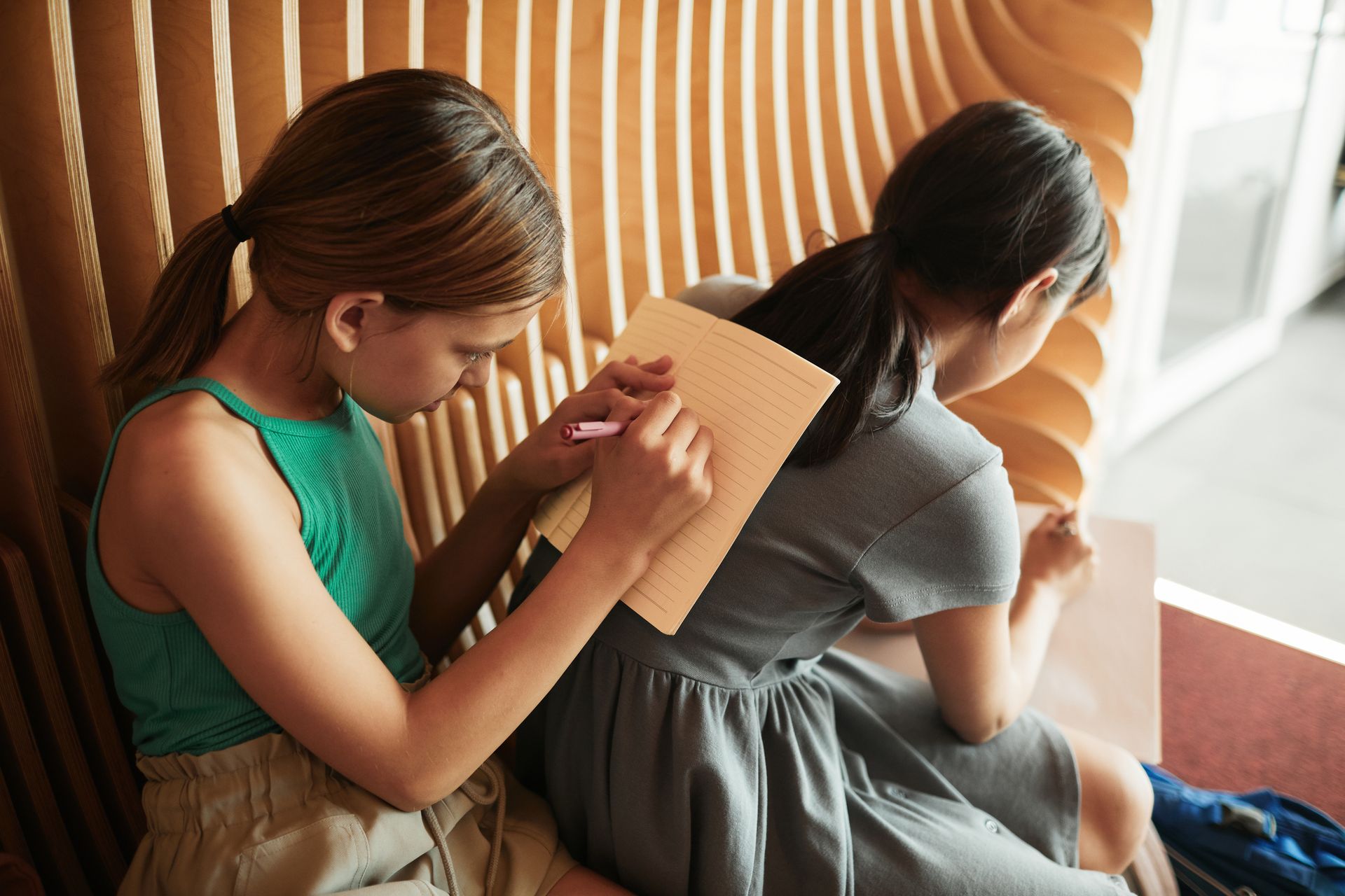 Two young girls writing on notebooks indoors, capturing a moment of focused learning.